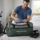 Man packs clothes into a green Krakow Duffle Bag labeled "Your Logo Here" on a bed.