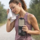 Woman wipes sweat with Easy Carry Compact Gym Towel, holding YOUR LOGO HERE mesh bag outdoors.
