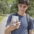 Teen boy with backpack smiles at phone; Phone Gripper Slides holder reads Your Logo Here.