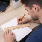 Man drawing a line in a notebook with a pencil and 30Cm Wooden Rulers at his desk.