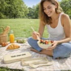 Smiling woman picnics on grass, enjoying fruit salad with Zaire Cutlery Sets.