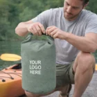 Man kneels by kayak, sealing a gray Huxley Dry Bags - 10L marked YOUR LOGO HERE.