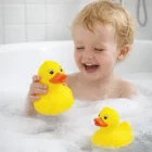 Smiling child in bubble bath with Squishy Rubber Ducks, holding one and another floating nearby.
