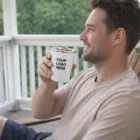 Man on a porch smiles, holding an Enamel Tumbler displaying YOUR LOGO HERE text.