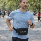 Man jogging in park wears a light blue shirt and an Axton Belt Bag with YOUR LOGO HERE.