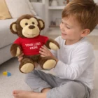 Smiling boy holds a Monkey Promo Branded Plush Toy wearing a red YOUR LOGO HERE shirt.