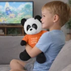 Smiling boy on couch holding Panda Branded Plush Toy with Your Logo Here on its shirt.