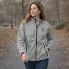 Woman in a park wearing a light gray Sols Relax Softshell Jacket with Your Logo Here.