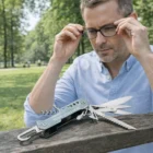 Man adjusts glasses in a Leipzig park, Leipzig Multi-Tools on the bench in the foreground.