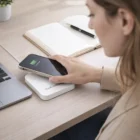A woman uses a Munich Wireless Chargers - Square at her desk with a notebook and laptop nearby.
