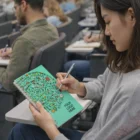 Woman writing in an A5 Full Colour Spiral Notebook during a lecture in a classroom.