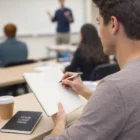 Student writes in a Moleskine Volant Journals Large; coffee cup and closed notebook on the desk.