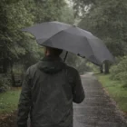 Person holding a Blunt Custom Umbrellas Xs Metro on a rainy, tree-lined path.