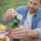 Man opening green bottle with Cap Style Branded Bottle Opener Keyring branded YOUR LOGO HERE.