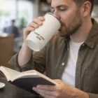 Man drinks from a Camelbak Horizon Vacuum Tumbler 500mL while reading at a cafe table.