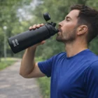 Man in blue shirt drinks from Camelbak Chute Mag Vacuum Bottles 1L in a green park.