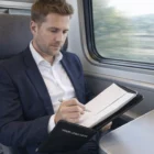 Man in a suit writes in Swiss Peak Heritage A5 Portfolio with zipper on train, folder says Your Logo Here.