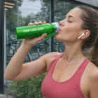 Woman in workout gear drinks outdoors from a Shiny Aluminium Bottle.