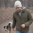 Man in Chaimheather Beanie and winter jacket walking a dog on a leash in a park.