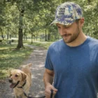Man in blue shirt walks dog, wearing a Jax Custom Caps hat reading "Your Logo Here.