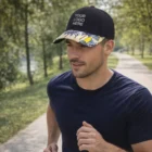 Man jogging in a park wearing a Jett Custom Peak Cap with YOUR LOGO HERE and a floral brim.