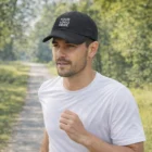 Man jogging outdoors in a white shirt and a black Rushcliffe Cap with YOUR LOGO HERE.
