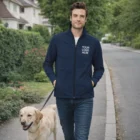 Man walks dog wearing a Sols Race Mens Softshell Jacket with "Your Logo Here" printed on it.
