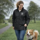 A woman wearing a Sols Shift Windbreaker walks her dog on a tree-lined park path.