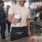 A barista wears a Lyra Denim Waist Apron featuring the text Your Logo Here.