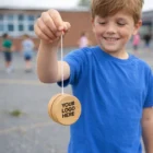 Smiling boy in blue shirt holding Colourful Logo Branded Wooden Yo-Yo outdoors.