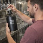 Man fills a Colson Beer Growler labeled "Your Logo Here" at a brewery tap station.