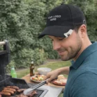 Man grilling sausages outdoors in Sussex, wearing a Sussex Bottle Opener Cap.