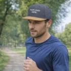 Man jogging in a park wearing a blue shirt and Kane Flat Peak Cap with YOUR LOGO HERE.