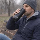 Man in a gray beanie enjoys his Swiss Peak Stealth Vacuum Mug on a park bench.