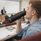 A student sips from a Swiss Peak Stealth Vacuum Bottle in a classroom during a lecture.