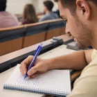 Man taking notes with Recycled Pet Logo Printed Pens during a lecture in a classroom.