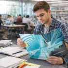 Young man at library table with Bulk A4 Presentation Folders With Spine and notes nearby.