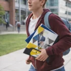 A student carries Promotional A4 Folders With Pockets and a backpack on a college campus.