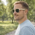 Man wearing Islington Basic Sunglasses Natura and a light blue shirt, outdoors in Islington park.