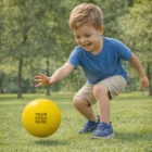 Smiling boy in blue shirt plays with a Bounz Hi-Bounce Ball on green grass outdoors.