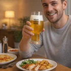 Smiling man holding Luigi Bormioli Birratique Beer Glasses with logo, food in front.
