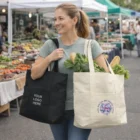 Woman at farmers market holds two Griesbach Canvas Tote Bags filled with fresh produce.