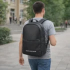 Man wearing a gray t-shirt and Swiss Peak Deluxe Backpack with Your Logo Here, walking outside.