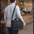 Man carrying a Swiss Peak RFID Laptop Bag enters a cozy café with wooden décor.