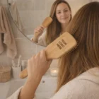 Woman uses Xyla Bamboo Hair Brush in front of mirror; "Your Logo Here" on brush.