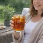 Smiling woman outdoors holding Hiball Drink Glasses with customizable logo.