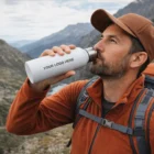 Man in hiking gear drinks from a Steveston Custom Branded Bottle in the mountains.