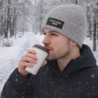 Man in Cumberland Heather Cable Knit Beanie Patches drinking coffee on a snowy winter day.