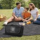 Family picnics on Swiss Peak Custom Picnic Blankets with drinks, fruit, and a basket.