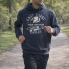 Man jogging in a park wearing a Lambton Unisex Hoodie with an eagle sports design.